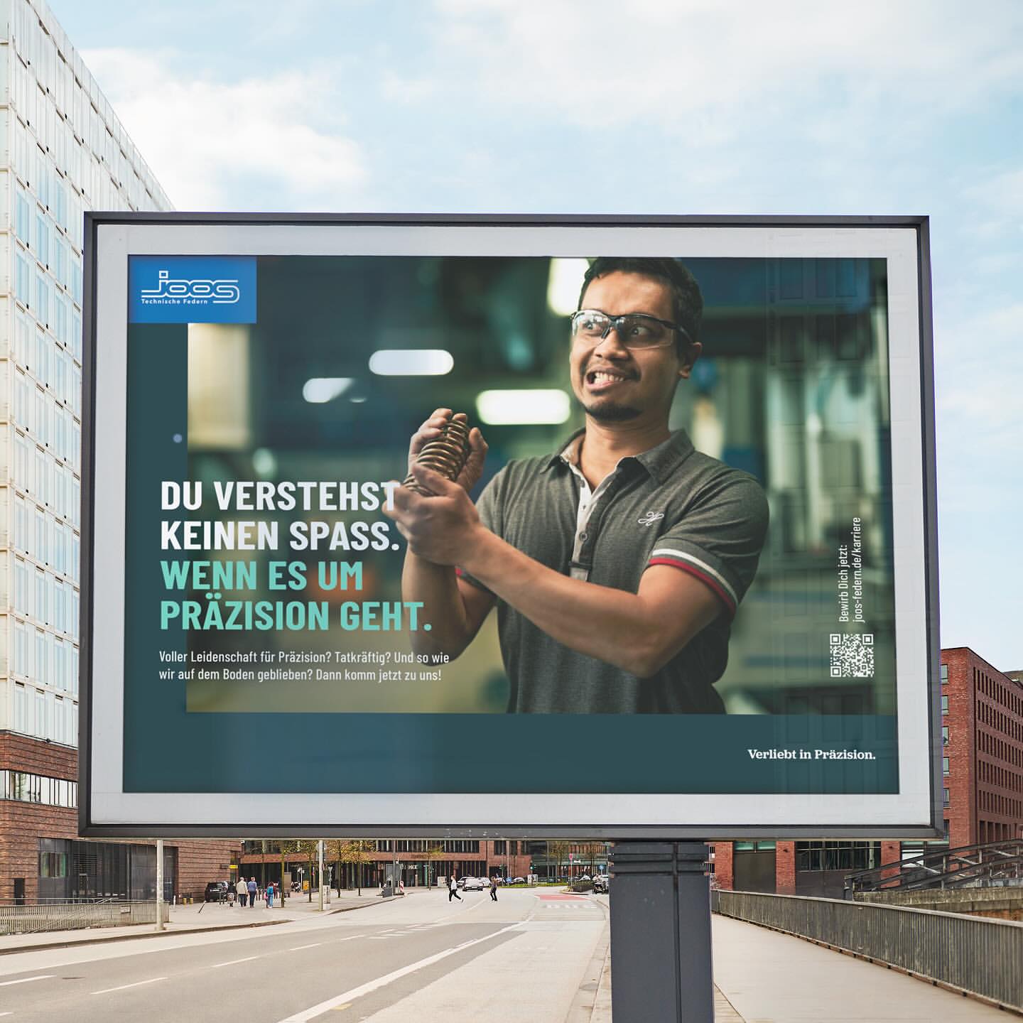 Billboard advertisement featuring a man straining while holding a spring, promoting precision engineering with visible urban background.