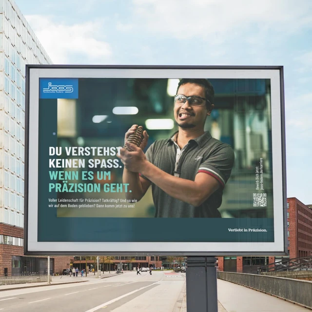 Billboard advertisement featuring a man straining while holding a spring, promoting precision engineering with visible urban background.