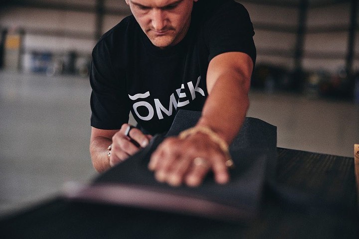Adult male smoothing black material with his hands, wearing a black t-shirt with white text. He is wearing gold wrist jewelry.