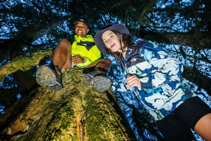 Two hikers perched high on a mossy tree trunk shot from a low worm eye view angle in a forest by Michael Kunde