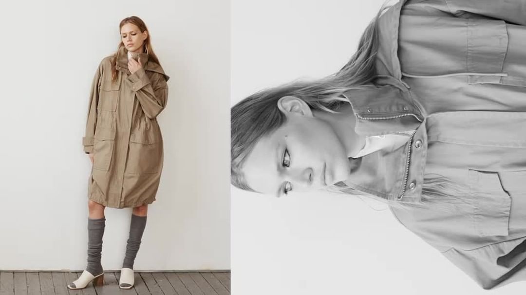 A woman stands in a long tan coat and gray socks with heels, in a studio setting against a white wall, in a fashion editorial image.