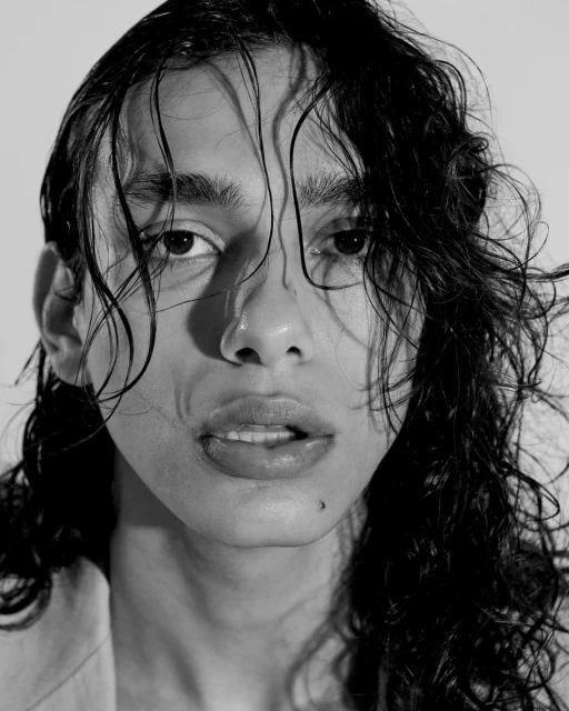 Close-up portrait of a young adult with dark, wet hair against a white background in black and white, showcasing a modern aesthetic.