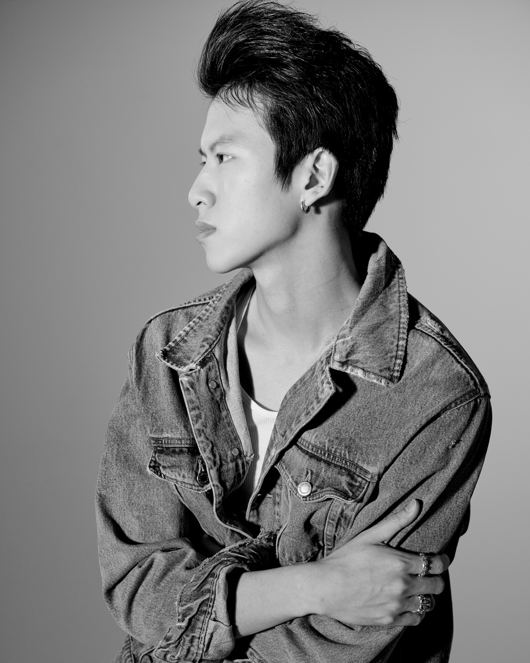 Monochrome portrait of an Asian man with pompadour, wearing a denim jacket, shot against a simple studio backdrop with even lighting.