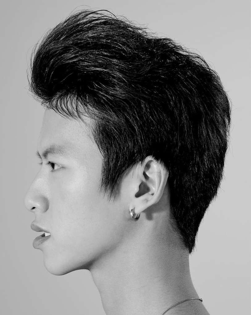 Black and white studio portrait of a young adult Asian male with swept-back hair, earring, and visible neck and collarbone.