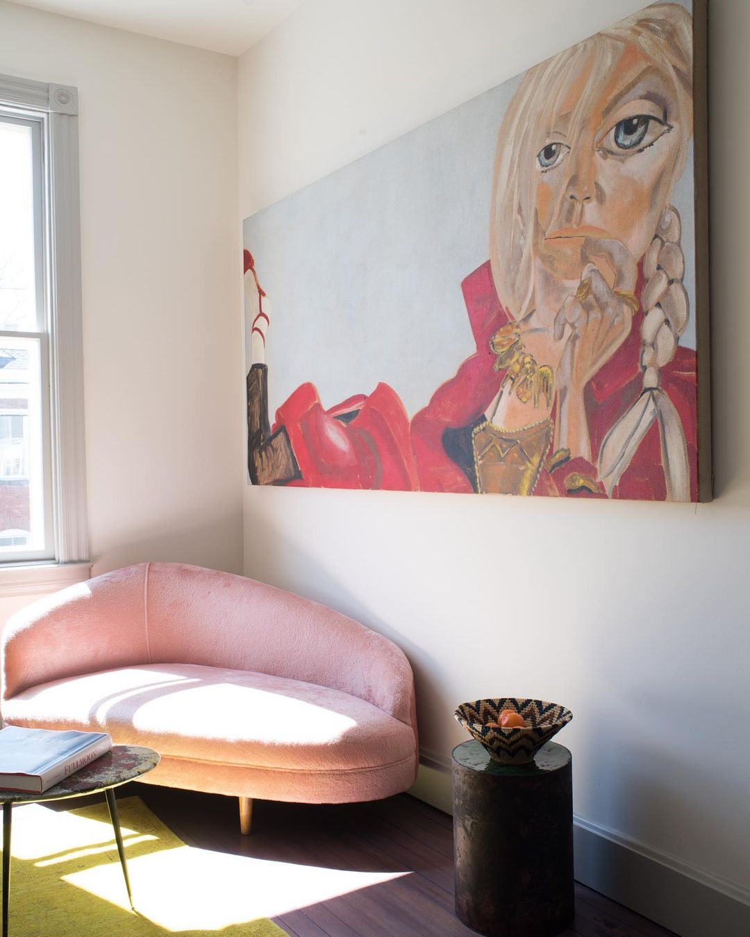 Interior view of a room with pink settee, side table, dark flooring, and a large painting of a woman hanging on the wall.