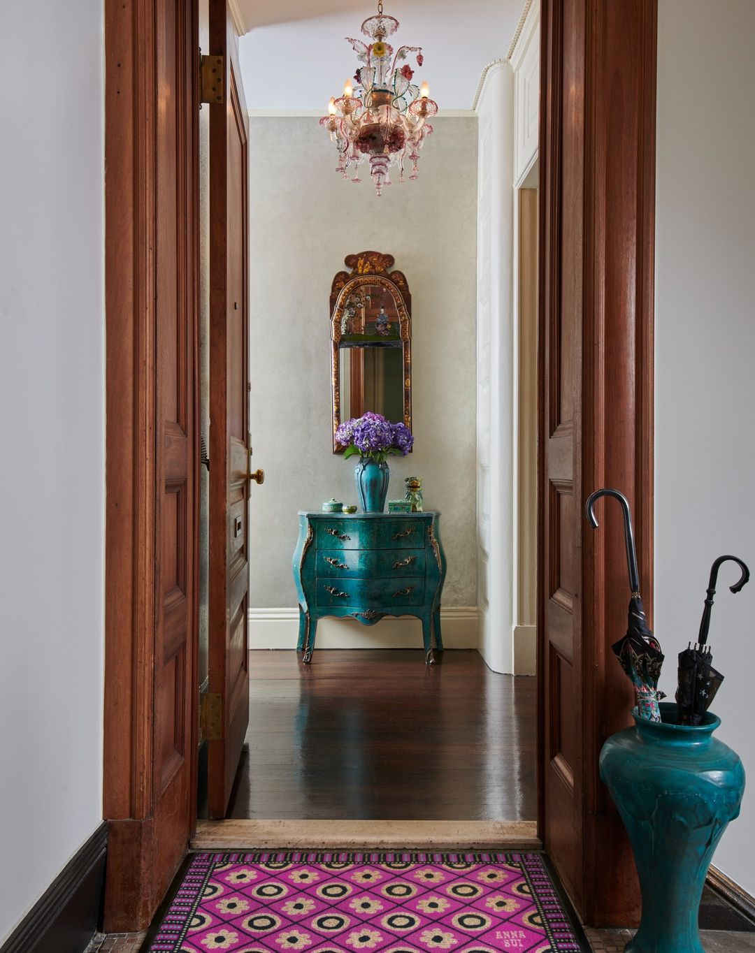 Interior of home featuring a foyer with hardwood floors, a colorful rug, turquoise dresser, and decorative mirror and chandelier.