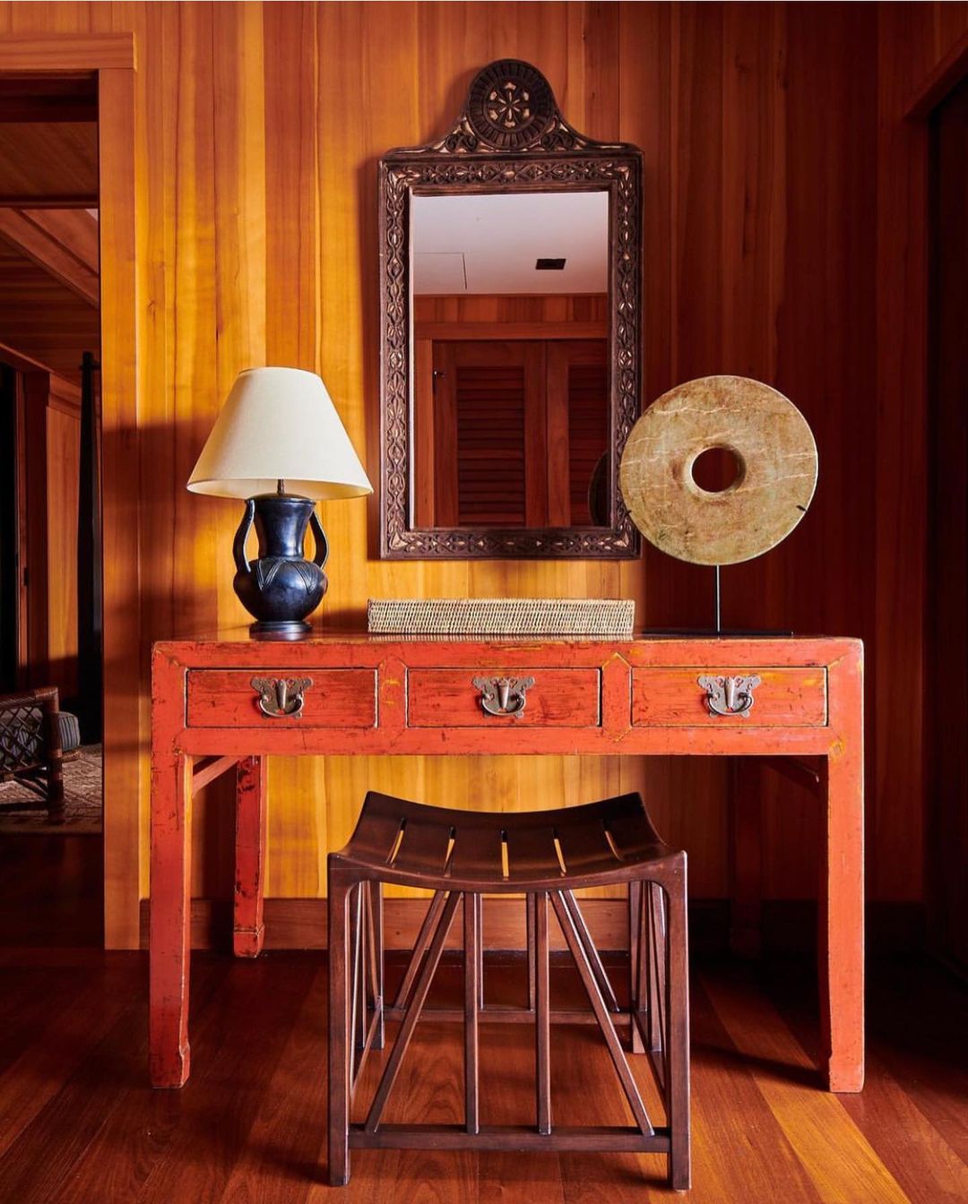 Interior view of a hallway with a console table with a mirror, a lamp, and a stool in front of a wooden paneled wall.
