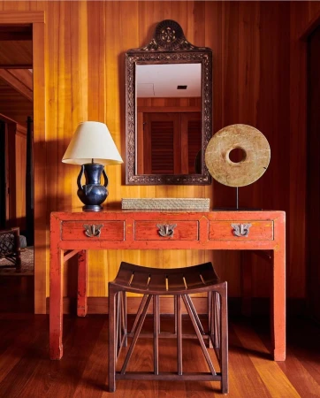 Interior view of a hallway with a console table with a mirror, a lamp, and a stool in front of a wooden paneled wall.