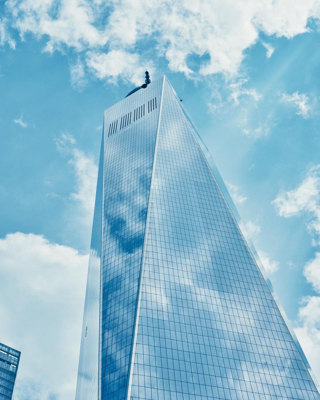 Low-angle view of modern skyscraper with glass facade reflecting sky and clouds. Tall building dominates composition.
