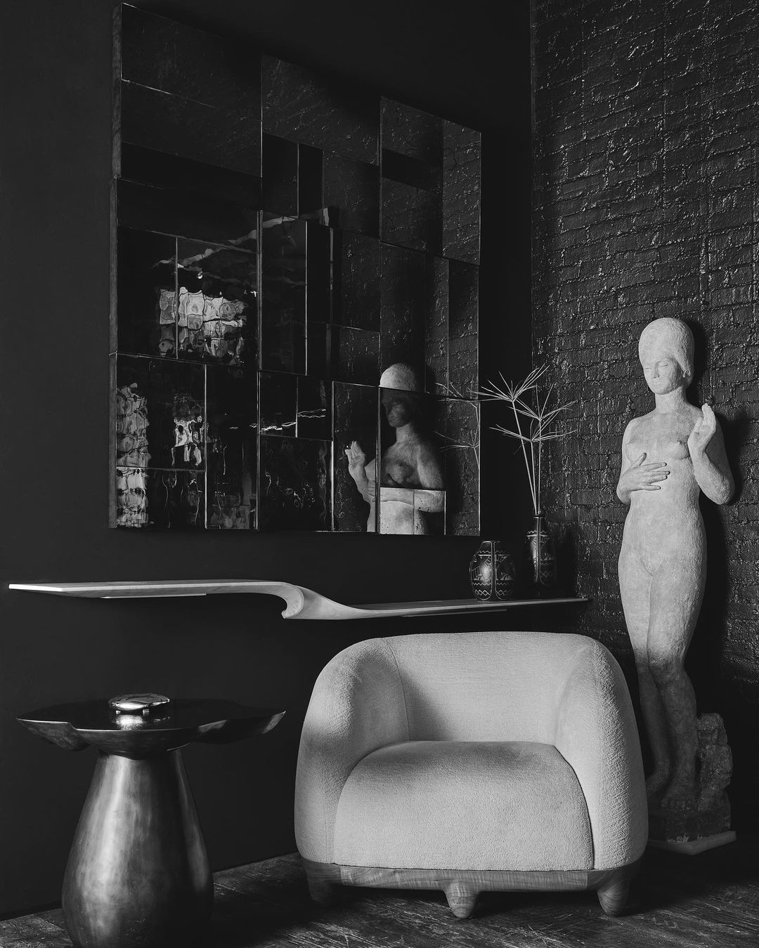 Interior shot featuring a white armchair, textured wall, a statue, a mirror, and a black accent table in a monochromatic setting.