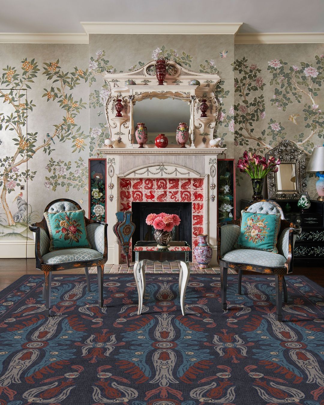 Interior shot featuring two matching armchairs with teal pillows flanking an ornate fireplace with floral wallpaper and mantelpiece by Michael Mundy.