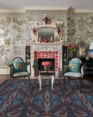 Interior shot featuring two matching armchairs with teal pillows flanking an ornate fireplace with floral wallpaper and mantelpiece by Michael Mundy.