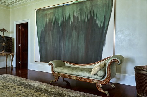Interior view of a formal living room with a chaise lounge, dark wood floors, and a large abstract painting on the wall.