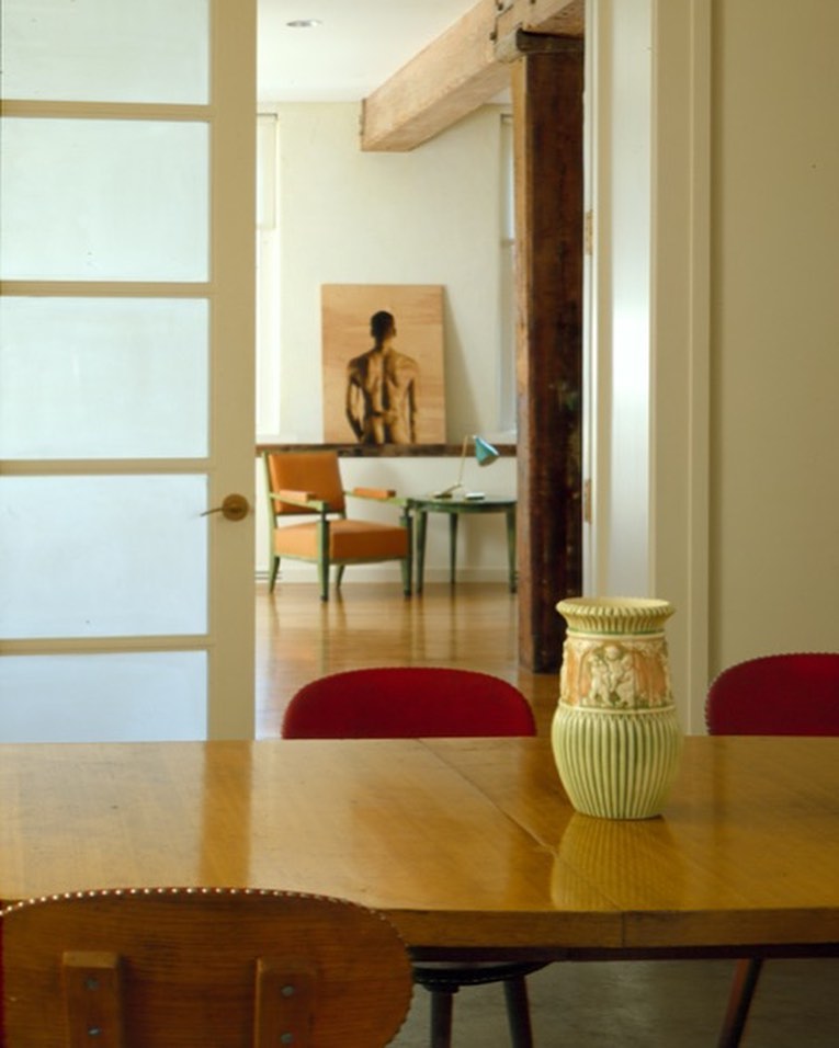 Interior view of a dining room with a wooden table, red chairs, and a decorative vase, seen through a doorway into a living area.