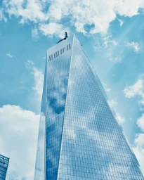 Low angle view of One World Trade Center skyscraper against a bright blue sky with white clouds in New York City.