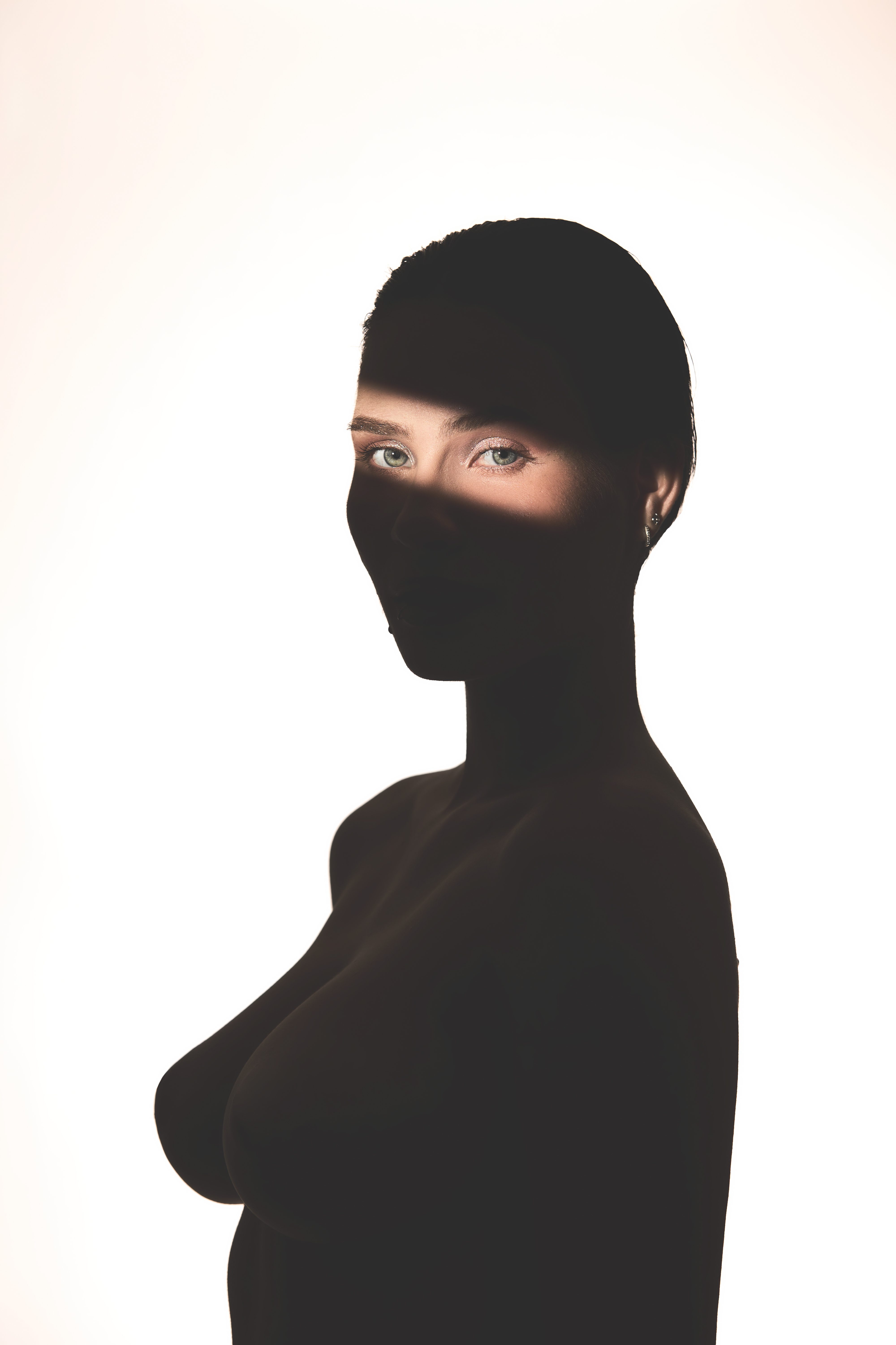 High-contrast silhouette portrait of a woman against a white background with a narrow beam of light illuminating only her eyes.