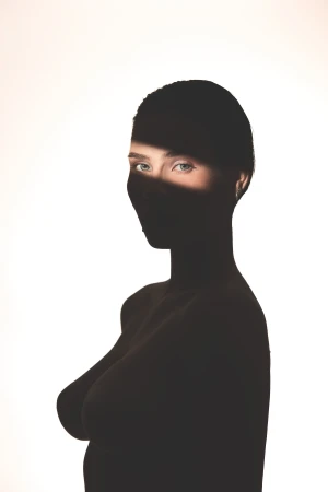 High-contrast silhouette portrait of a woman against a white background with a narrow beam of light illuminating only her eyes.