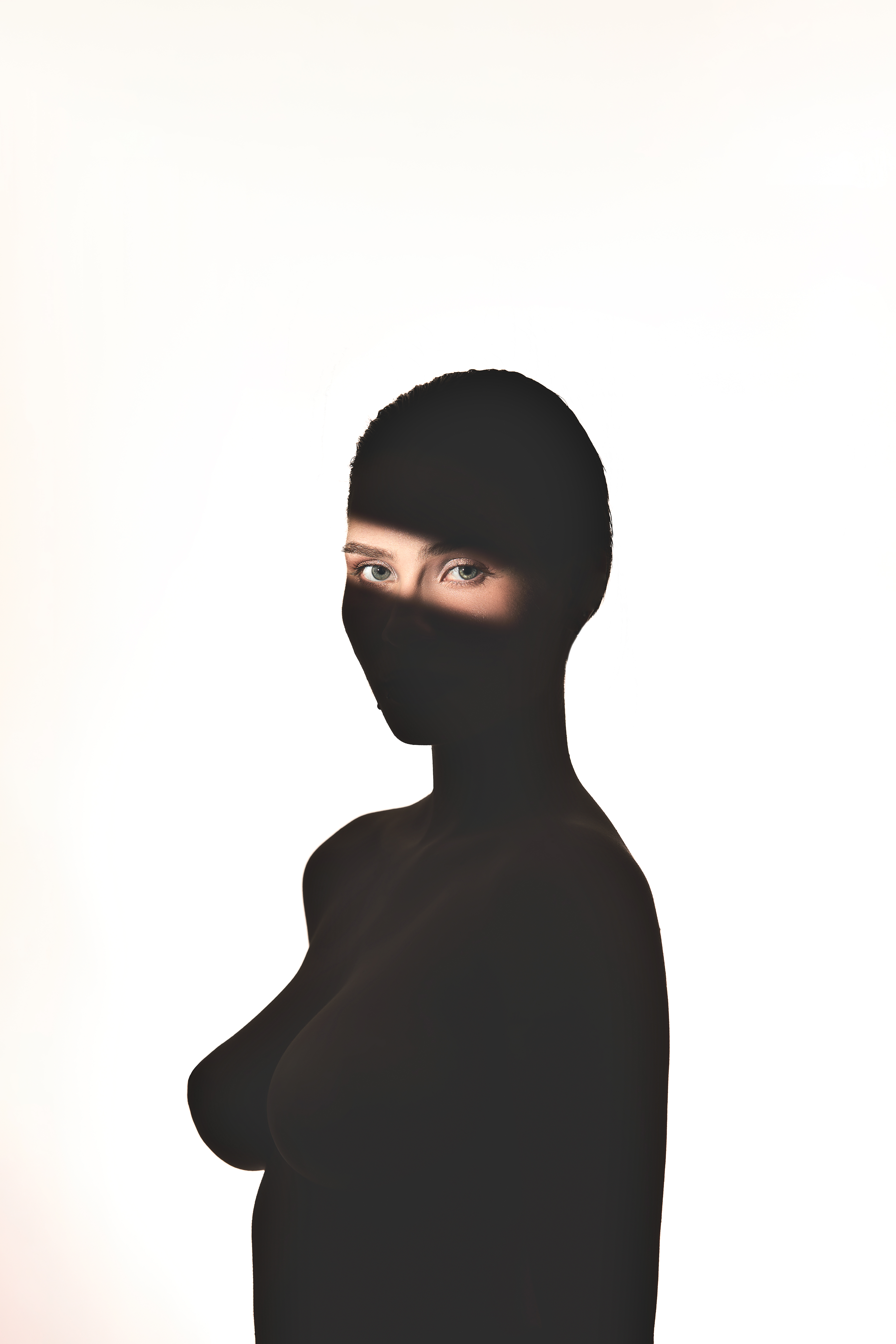 Portrait of a woman wearing a black balaclava with a bright horizontal slash of light across her eyes against a white background.