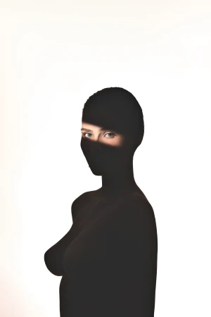 Portrait of a woman wearing a black balaclava with a bright horizontal slash of light across her eyes against a white background.