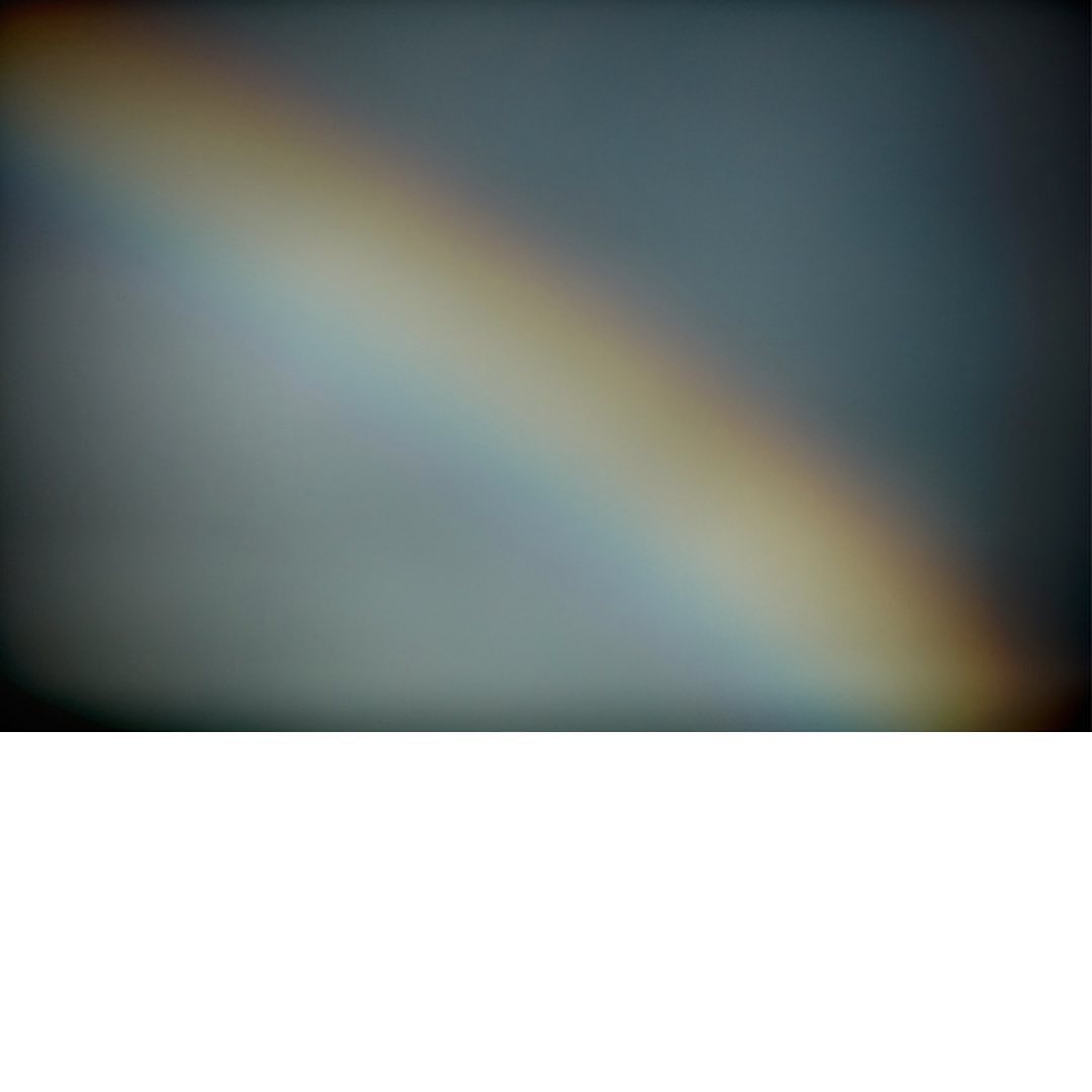 A vibrant diagonal rainbow arc dominates the frame against a softly blurred, gradient background, creating a luminous, atmospheric effect.
