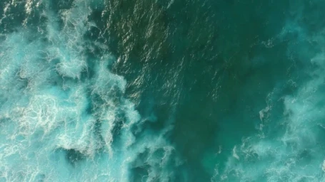 Top-down aerial view of turquoise ocean water with white foamy waves crashing across the surface.
