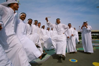 Group of men in white thobes and headscarves performing a traditional dance outdoors under a blue sky.