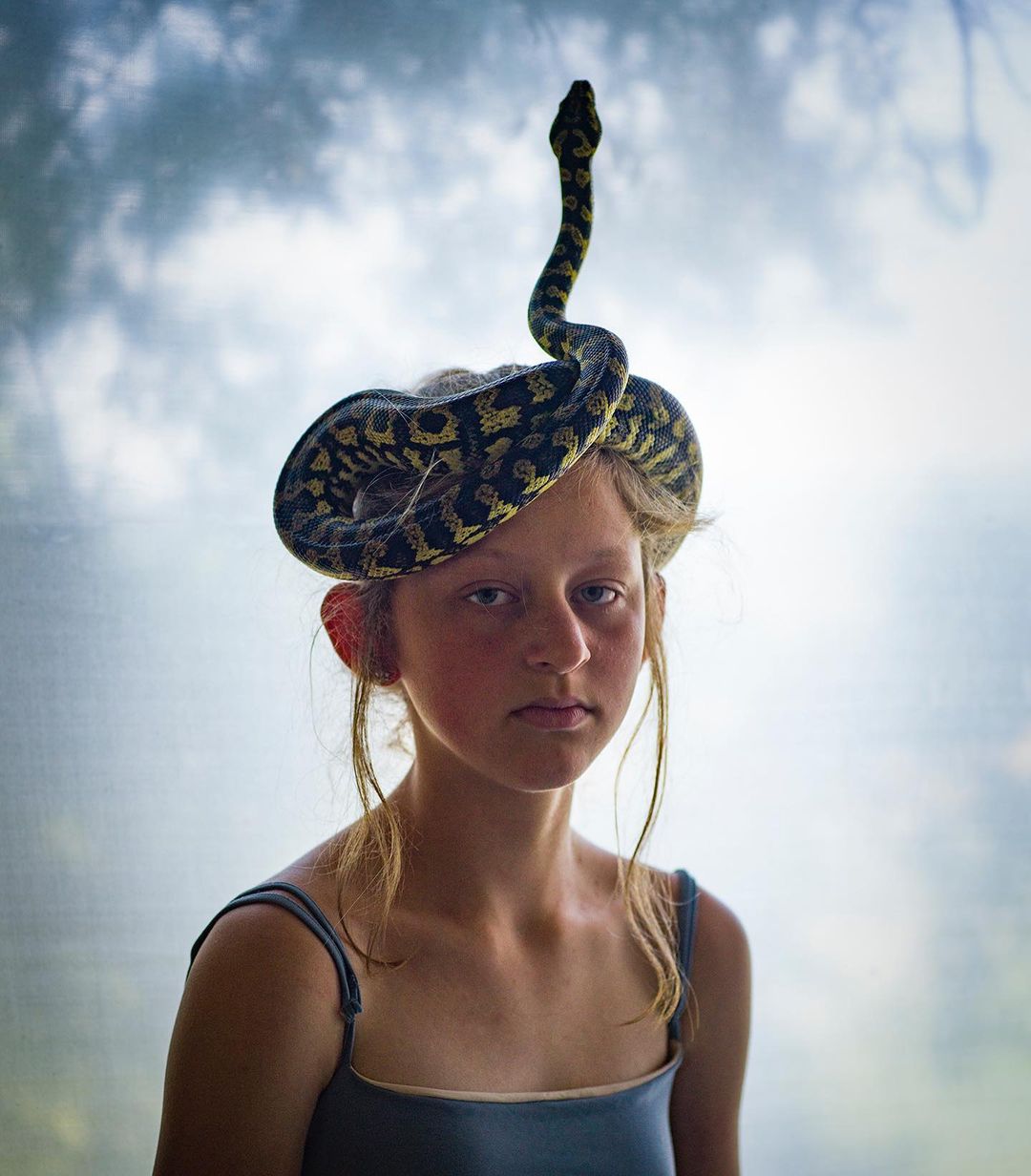 Portrait of a young girl wearing a snake as a hat against a blurred background, showcasing a unique and striking visual.