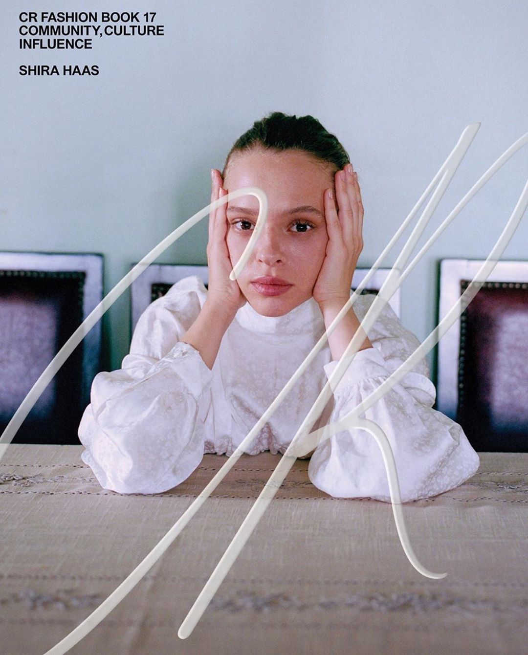Editorial fashion shot featuring a young woman with hands on her face, white textured top, and abstract white line design.