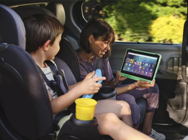 Young woman and boy sitting in the backseat of a car, looking at a bright green tablet screen while traveling.