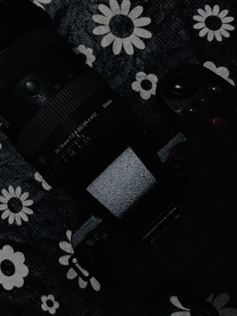 Close-up of a black camera and lens resting on a dark patterned fabric background with white flower motifs.