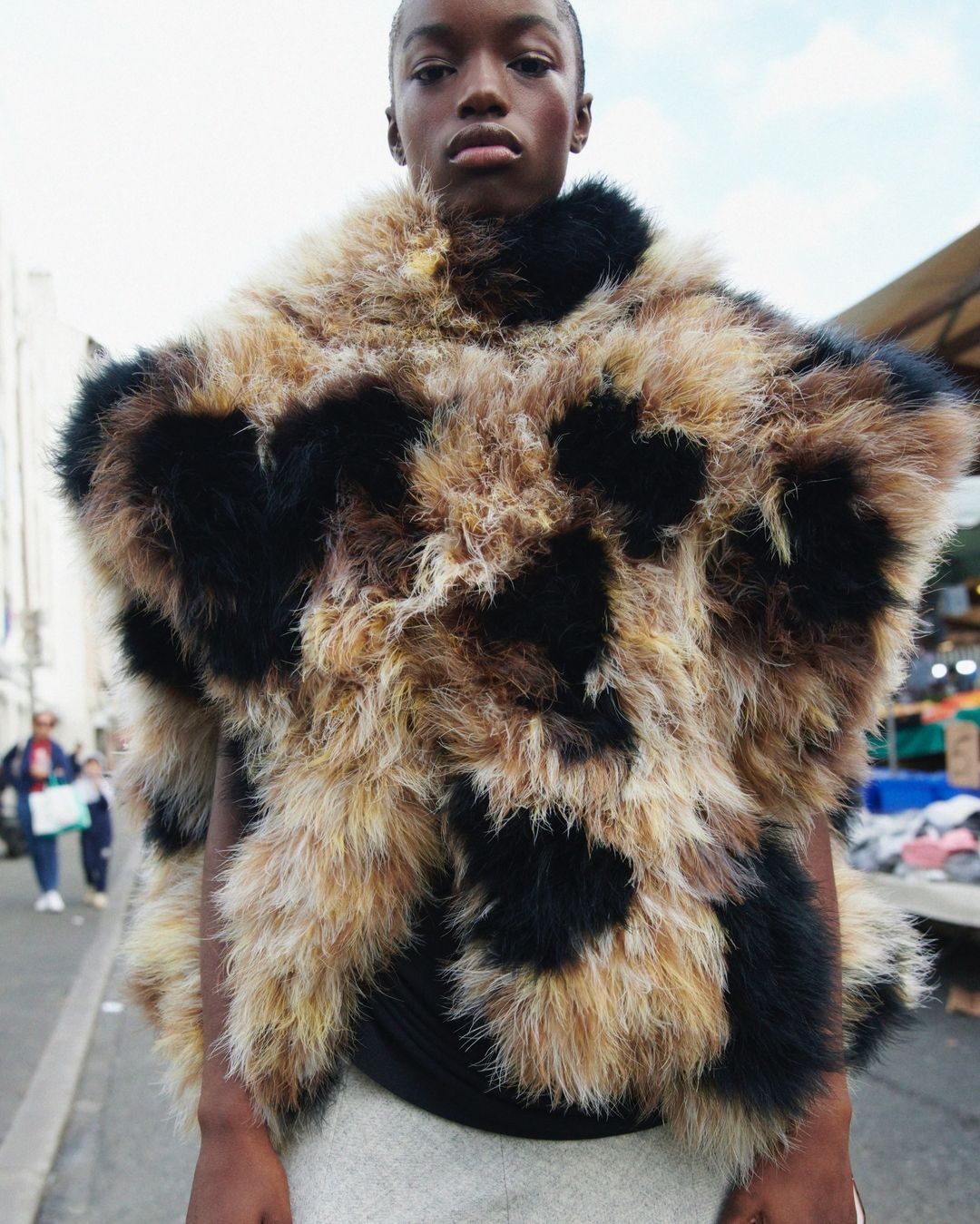 Young woman wearing a fur poncho in an outdoor setting. Street style fashion with a unique and textured garment in a candid pose.