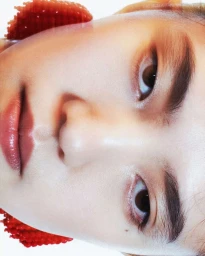 Close-up portrait of a woman wearing textured red earrings against a light background, photographed by Mickael B Schnitzer.