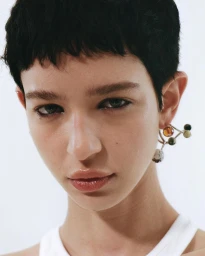 Close-up portrait of a woman with short dark hair wearing a sculptural jewelled earring against a white background