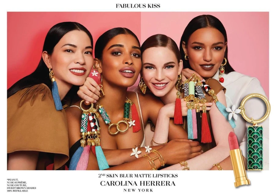 Group of four smiling women with various skin tones are closely grouped together, displaying jewelry, lipstick, and fashion accessories on pink background.