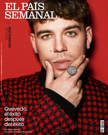 Magazine cover portrait featuring a young adult male with brown hair wearing a red and black checkered jacket and jewelry, set against a red background.