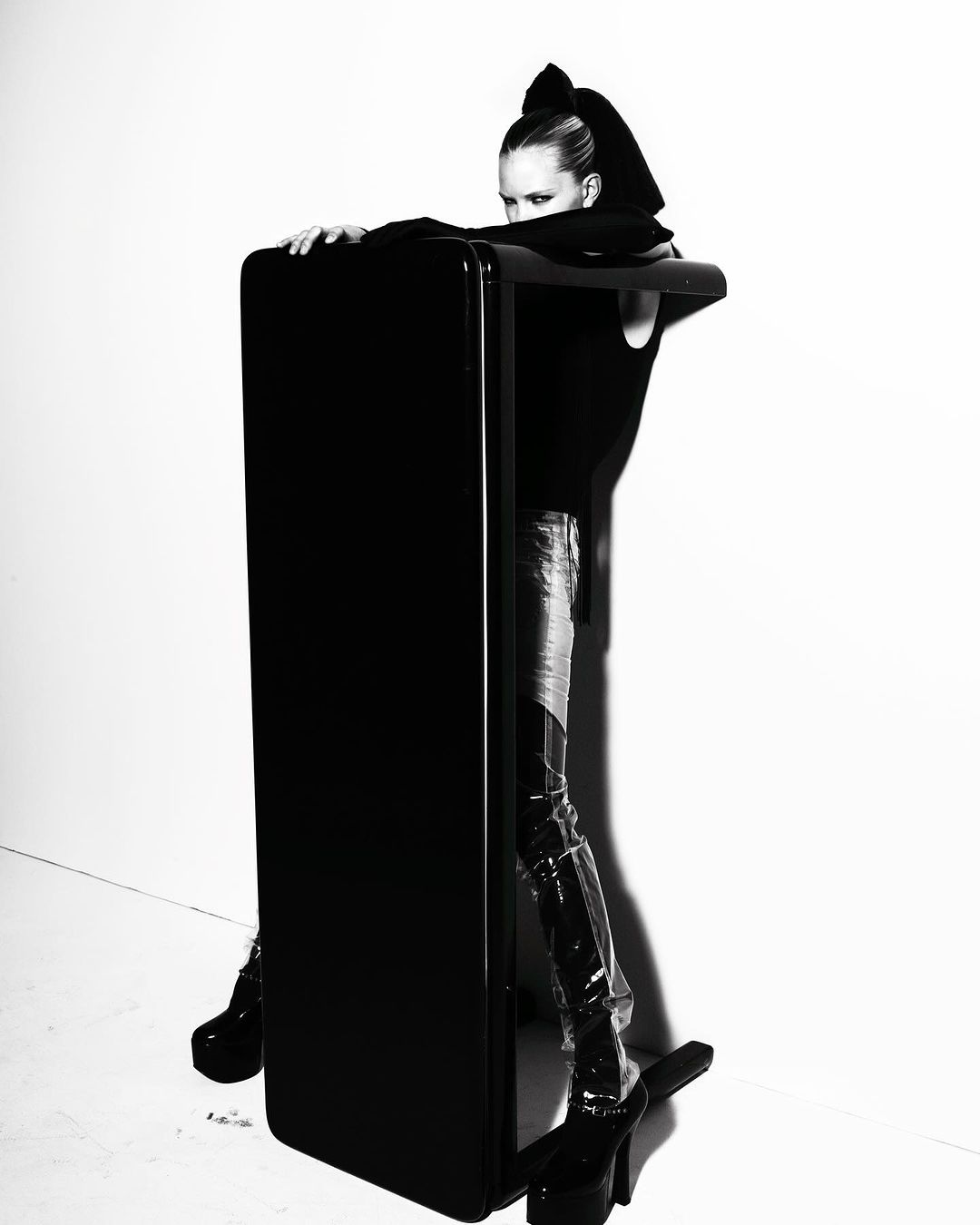 High contrast studio shot of a model in glossy boots leaning on a sleek, modern treadmill against a bright white backdrop.