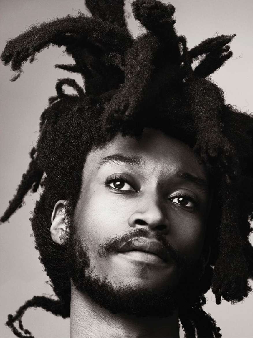 Portrait of a man with dreadlocks in a close-up shot, showcasing the texture of his hair and facial features against a neutral backdrop.