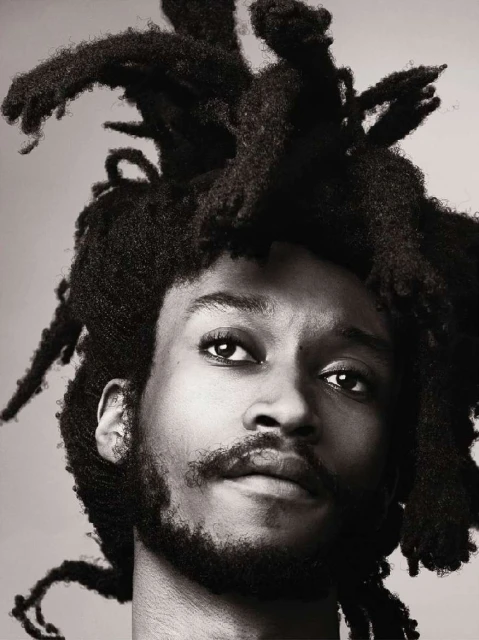 Portrait of a man with dreadlocks in a close-up shot, showcasing the texture of his hair and facial features against a neutral backdrop.