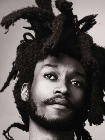Portrait of a man with dreadlocks in a close-up shot, showcasing the texture of his hair and facial features against a neutral backdrop.
