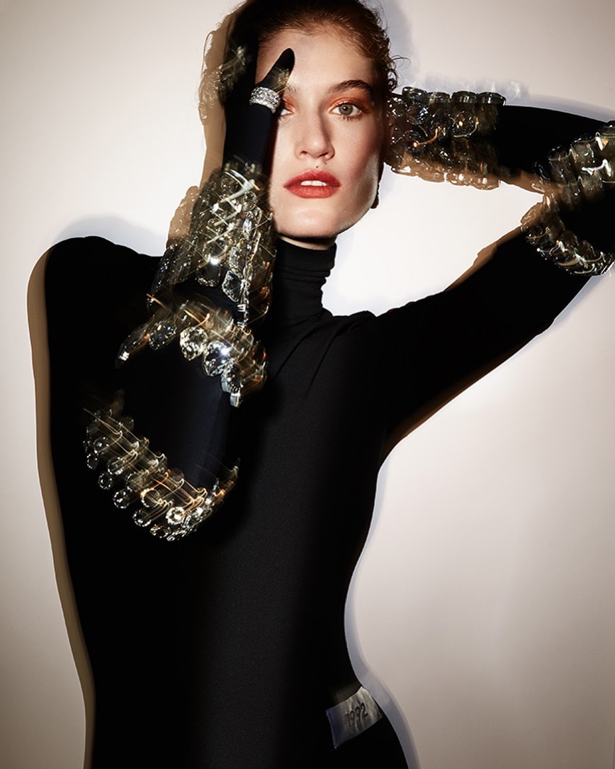 Model in black turtleneck wearing ornate crystal embellished cuffs posing against a light background