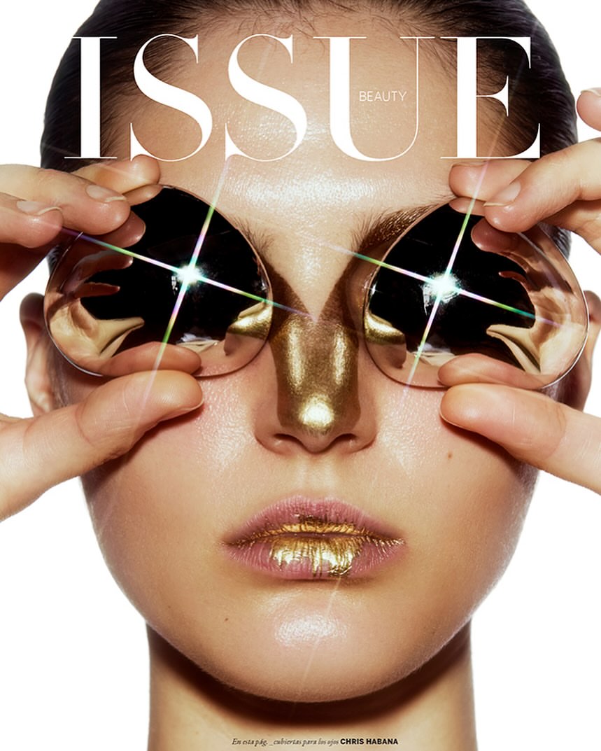 Beauty editorial featuring a woman with metallic gold makeup, holding reflective objects over her eyes on a white backdrop.