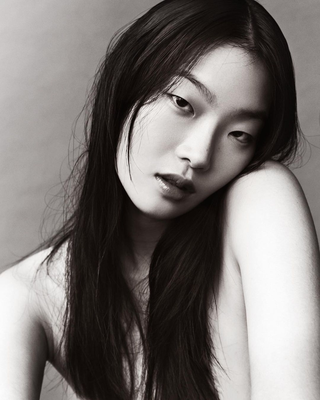 Close-up portrait of an East Asian woman with long dark hair posing against a neutral grey studio background by Mikael Schulz.