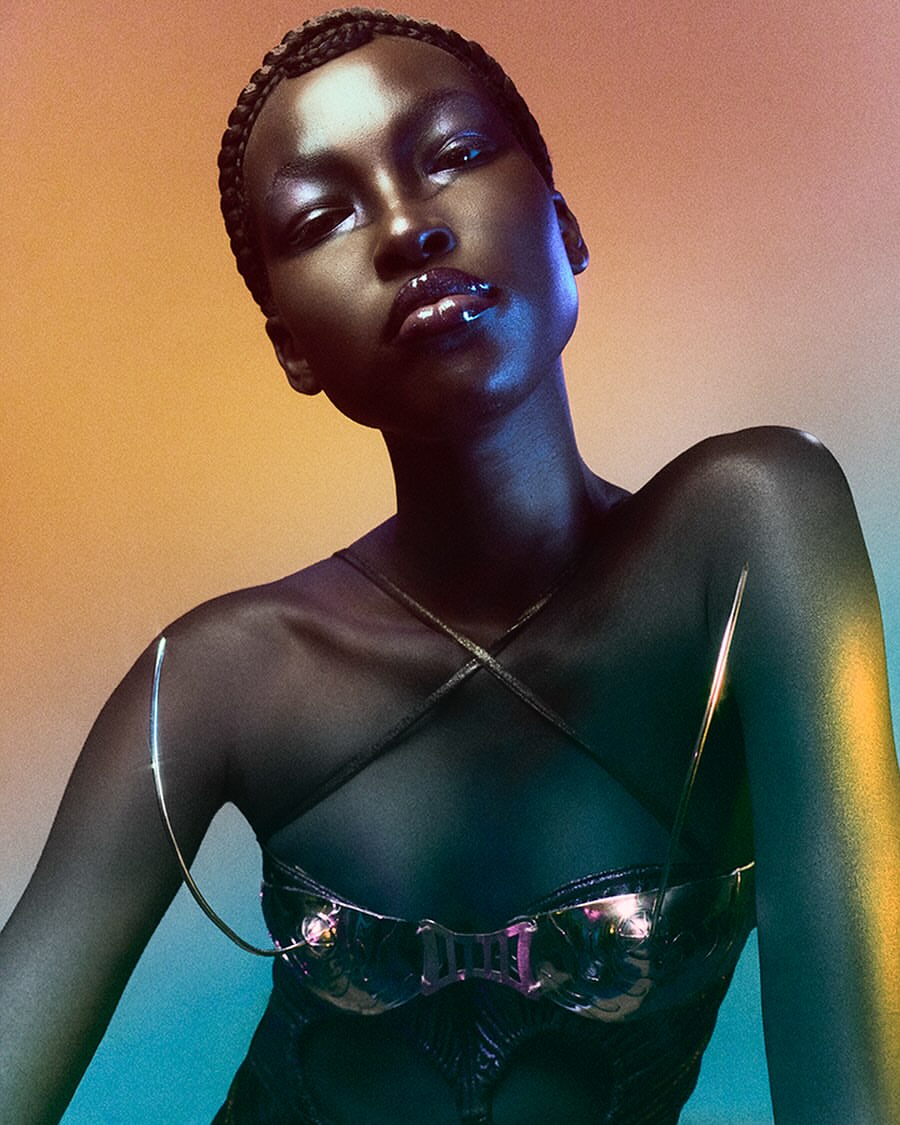 Close-up portrait of a woman with dark skin, metallic bra, and glossy makeup against a gradient background. Fashion, beauty, and studio shot.