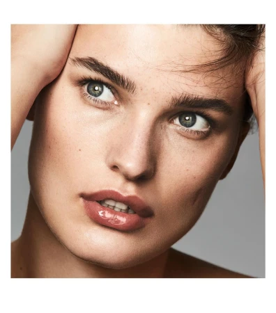 Close-up beauty portrait of a woman holding her hands to her head with glossy lips and freckles against a neutral background