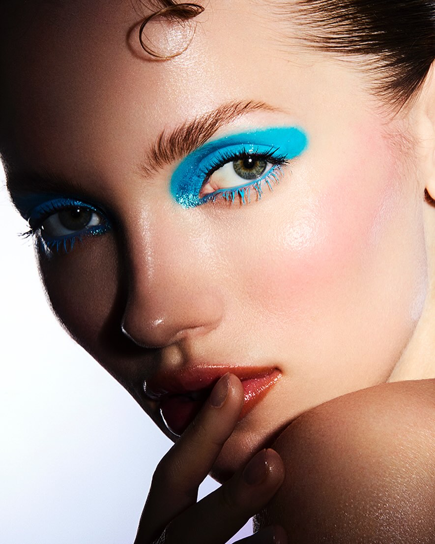 Close-up beauty shot of a woman with glossy lips and bright blue eyeshadow. Beauty and makeup concept for cosmetic advertising.
