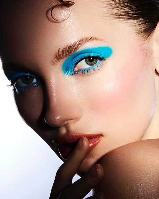 Close-up beauty shot of a woman with glossy lips and bright blue eyeshadow. Beauty and makeup concept for cosmetic advertising.