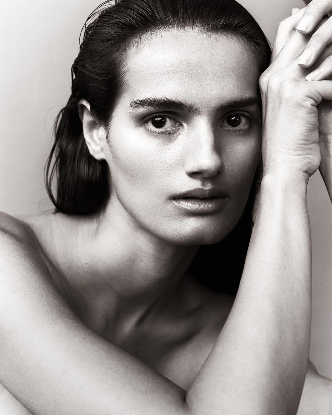 Close up portrait of a woman with wet hair posing with hands pressed against her cheek by Mikael Schulz