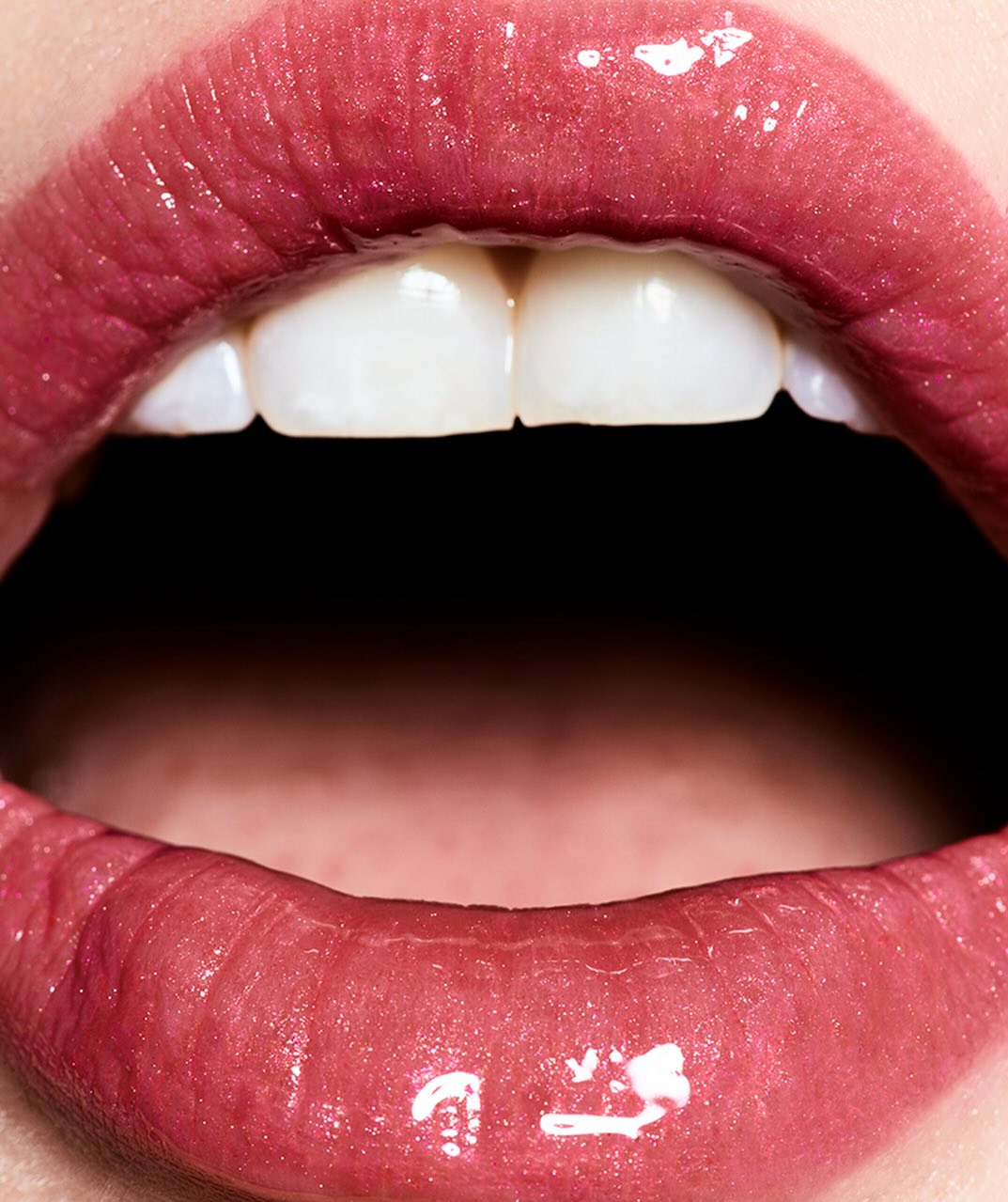 Macro photograph of an open mouth revealing teeth. Focus on glossy lips and teeth in a beauty close-up for cosmetic concept.