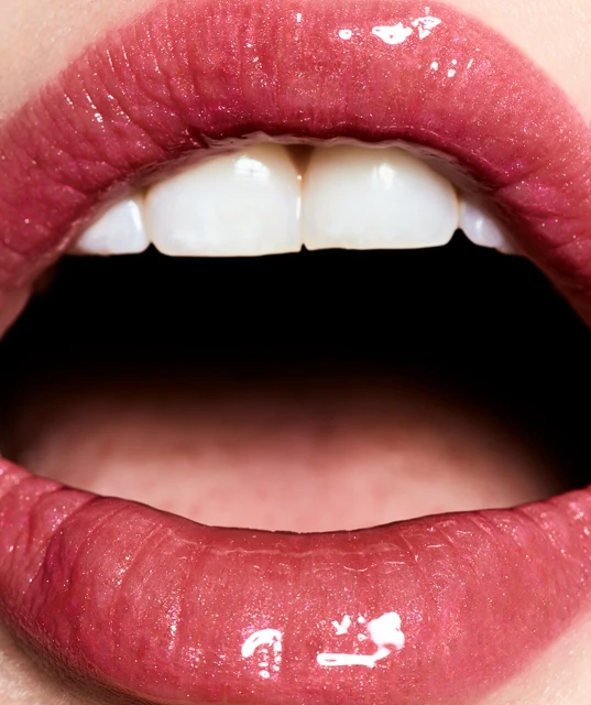Macro photograph of an open mouth revealing teeth. Focus on glossy lips and teeth in a beauty close-up for cosmetic concept.