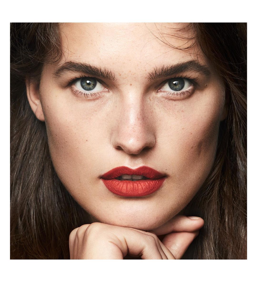 Close-up of a woman with fair skin, red lipstick, and dark brown hair. Portrait shot with soft lighting, emphasizing her facial features.